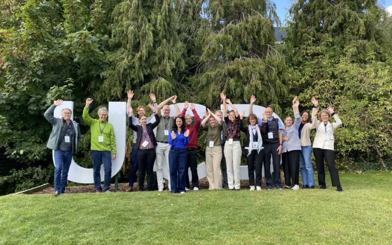 Members of TheRaCil consortium posing and waving (like cilia) in front of University College Dublin sign during the Cilia2024 international conference.